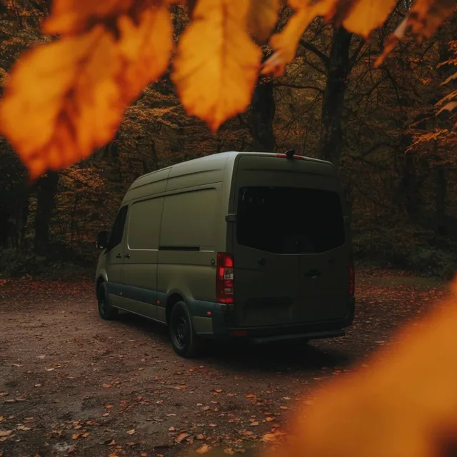 matte olive green camper van in an autumn forest, rear three-quarter view, dirt clearing scatte...