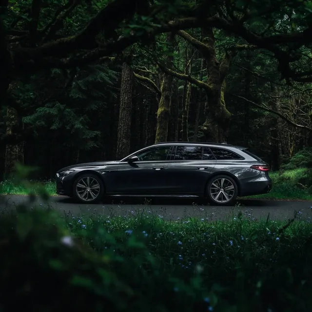 A sleek, dark grey modern station wagon parked on an asphalt road winding through a dense fores...