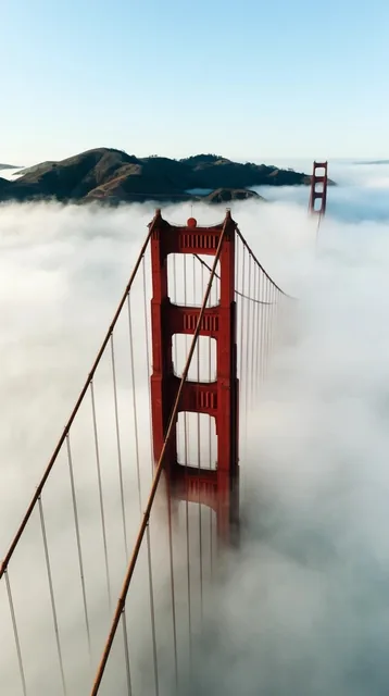 An aerial view captures the towering rust-red peaks of a massive suspension bridge piercing thr...