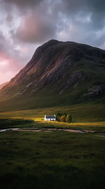 massive rugged mountain towering over a vast green valley, tiny isolated white cottage bathed i...