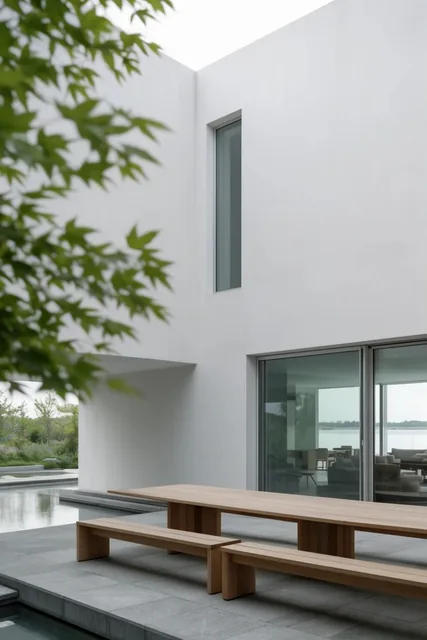 minimalist white architectural courtyard, long wooden table with benches on grey stone patio, s...