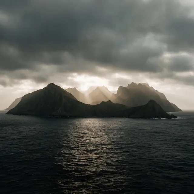 Dramatic wide landscape photography, rugged mountainous island surrounded by dark rippling ocea...