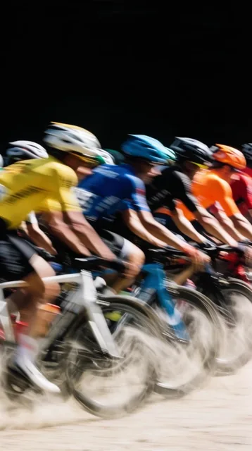 A tightly packed peloton of cyclists races forward in an extreme motion-blurred panning shot ag...