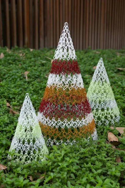 Three conical lattice structures built from interlocking plastic loops rest among lush green gr...