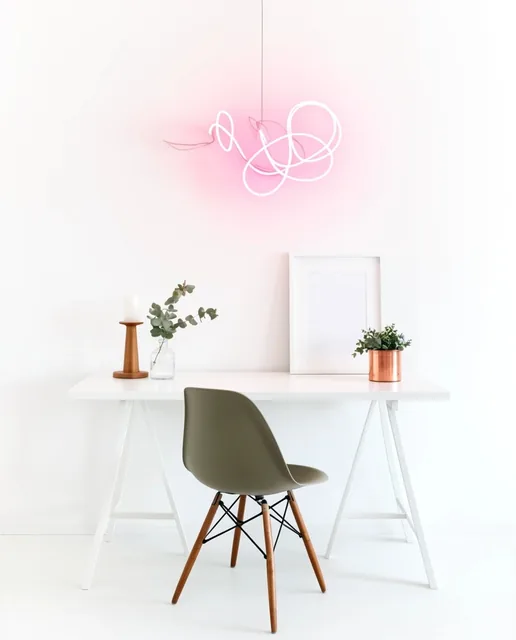 A minimalist workspace features a white trestle desk and an olive-grey molded chair against a s...