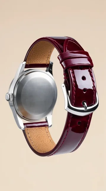 A silver wristwatch viewed from a rear three-quarter angle against a minimal beige background....