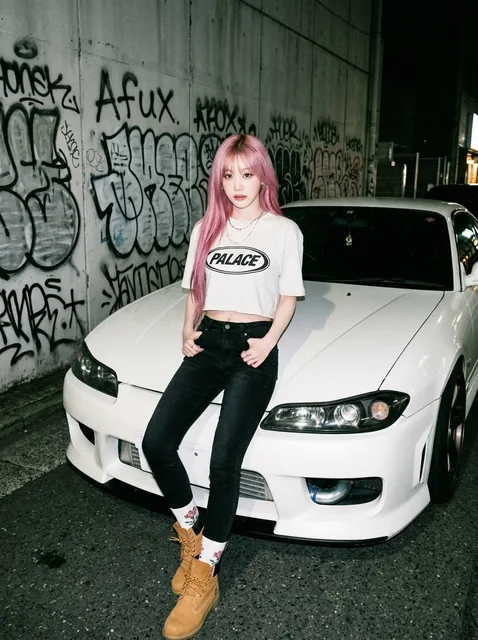 A young woman in a white cropped t-shirt, black denim shorts, and tan boots leans against a modified Nissan Silvia S15 at night, with graffiti in the background, captured in a 90s