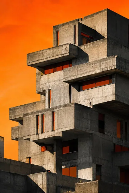 A massive brutalist concrete building with stacked geometric balconies, raw gray concrete texture, deep rectangular wind