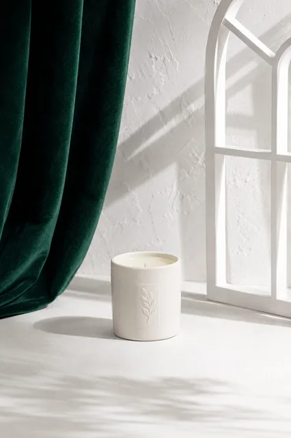 Minimal studio product photography, a small white candle centered on a white tabletop, textured white background, deep e