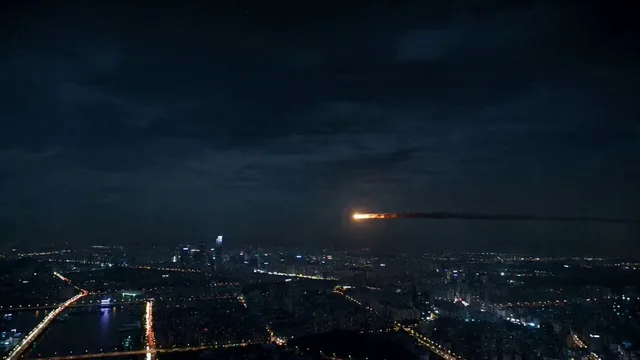 A glowing asteroid enters the atmosphere above a sprawling metropolis at night.
