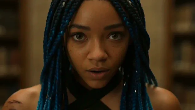 A 19-year-old woman with micro braids dyed deep indigo, warm brown skin, wearing a shredded athletic wrap top and cargo