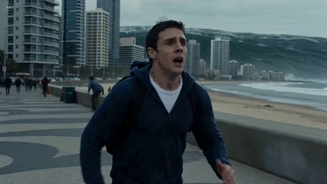 A man sprinting through a coastal city, panic in his eyes, water reflecting in the distance. Turns as a colossal tsunami