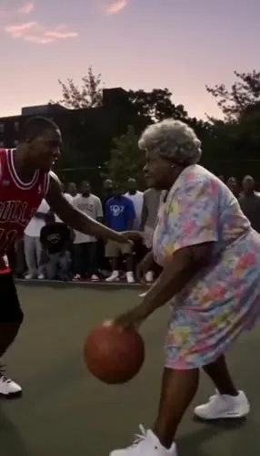 Shaky, grainy vertical video of an elderly woman in a floral dress performing a slam dunk at Rucker Park basketball court at dusk, with a crowd storming the court.