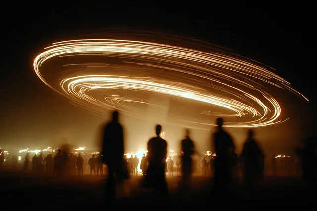 A ferris wheel on fire at night, with people watching.