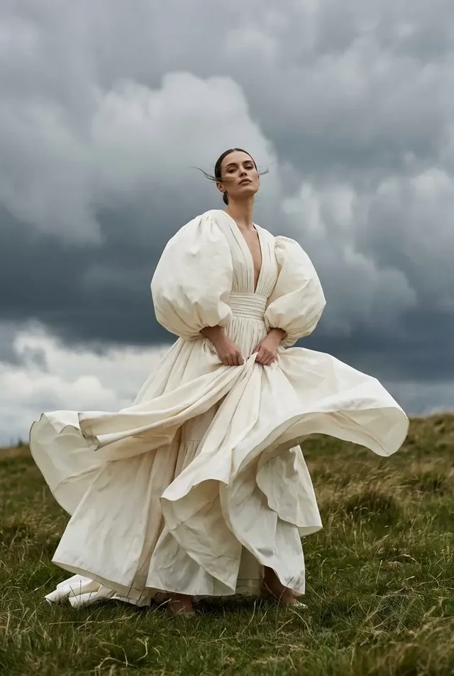 Ultra-realistic, wide cinematic shot of a woman in an ivory haute couture gown with balloon sleeves running across a grassy hill during a violent thunderstorm, with lightning striking in the distance.