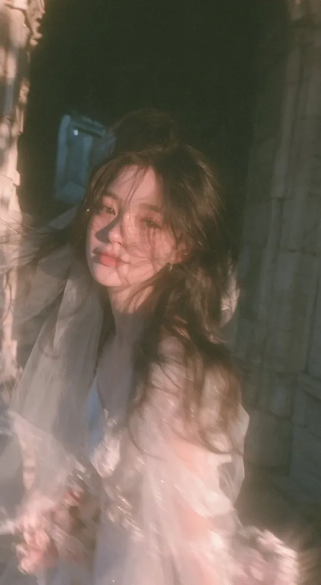 A candid vertical bridal portrait of a young East Asian bride in a lightweight white dress and veil, moving quickly through a sunlit European stone corridor with motion blur and warm Kodak Portra tones.