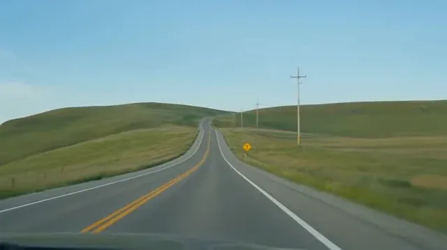 A group of friends on a road trip, laughing and taking photos at a scenic roadside pit stop, with a car and open road in the background. Authentic, handheld phone video style.