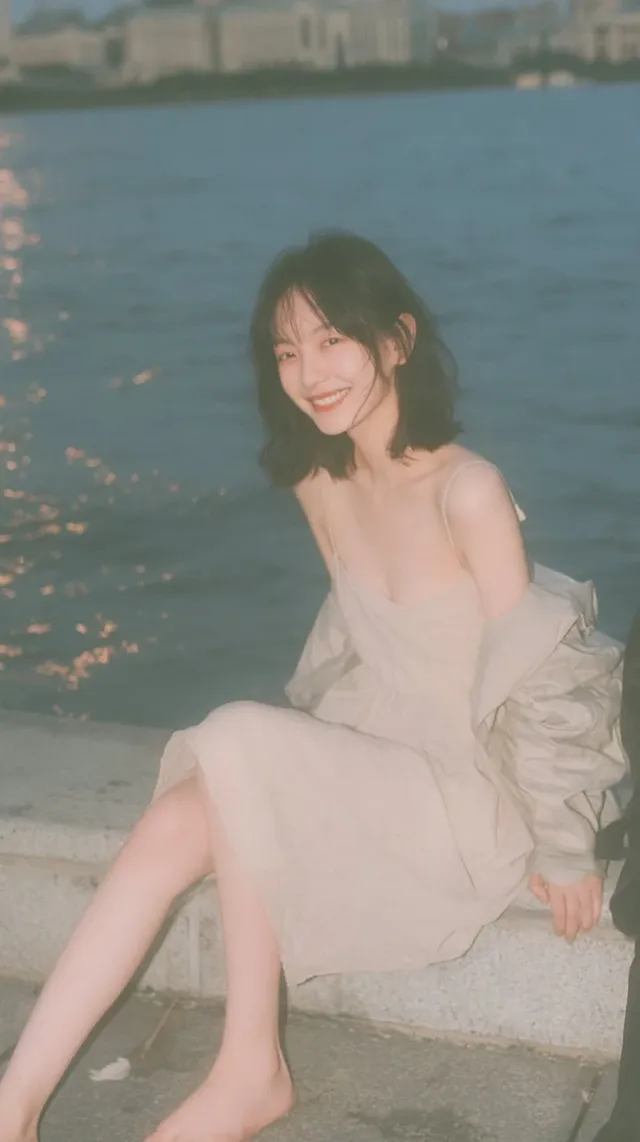 Photorealistic vertical full-body portrait of a young Japanese woman with black hair, wearing an apricot midi dress, sitting barefoot on stone steps by a river at dusk, smiling towards the camera.