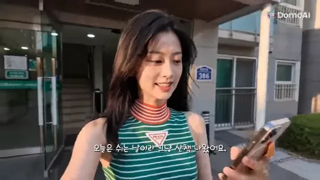 A young Korean woman with dark brown hair films herself with a smartphone, smiling at the camera during a walk.