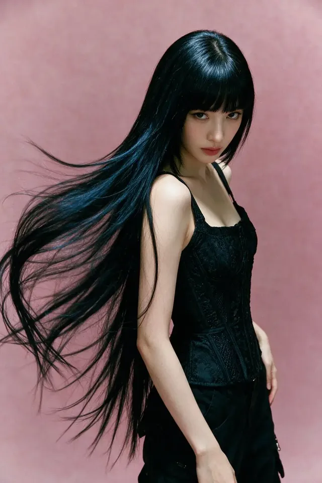 Fashion portrait of a woman with long jet-black hair and black corset against a muted dusty-pink studio wall.