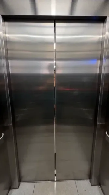 First-person view inside an elevator, watching the doors close, then frantically pressing the open button as a woman approaches in the hallway.