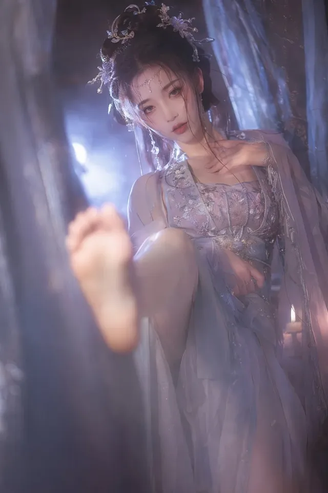 Photorealistic portrait of a pale Chinese woman in a blue-gray and silver hanfu, with elaborate hairpins, striking a graceful, low-angle kick with one bare leg towards the camera, in a soft-focus, moonlit, and candlelit haze.