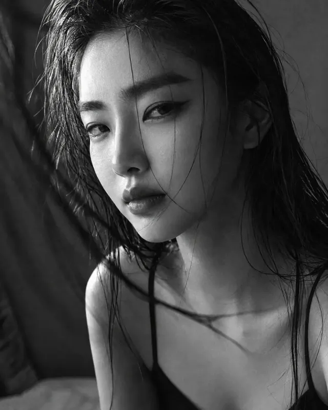 Black and white medium shot of a young Korean woman in a black slip dress and oversized blazer, with wet-slicked hair and a cool, detached gaze, featuring dramatic lighting and visible film grain.