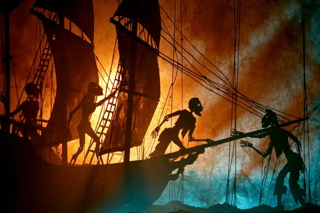 A shadow puppet theatre scene with jointed figures silhouetted against a glowing screen.