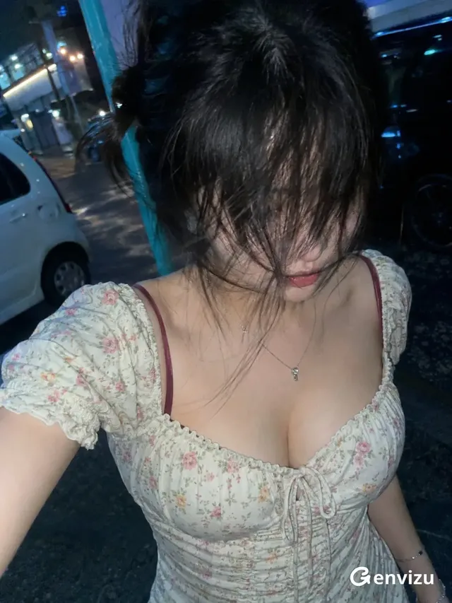 A young East Asian woman with black hair obscuring her face walks at night, captured in a grainy, high-angle handheld snapshot with a blue-green cast and motion blur.