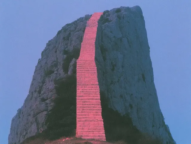 A surreal landscape with a pink staircase climbing a rocky mountain under a gradient blue sky.