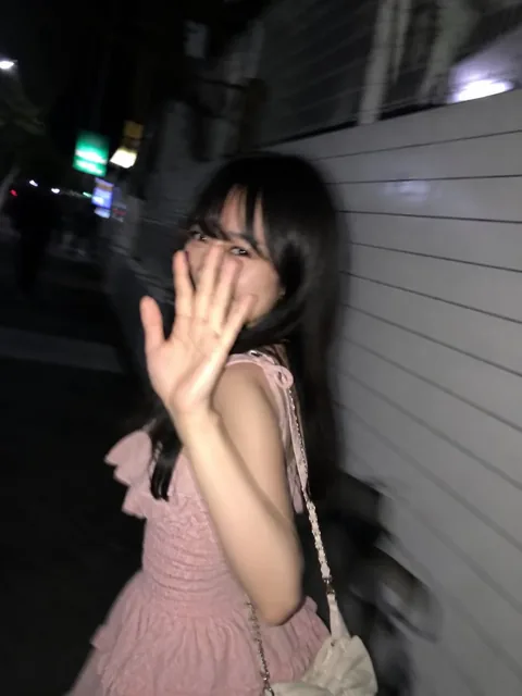 A young woman, blurred by motion, turns back with a shy smile on a dark Tokyo sidewalk at night.