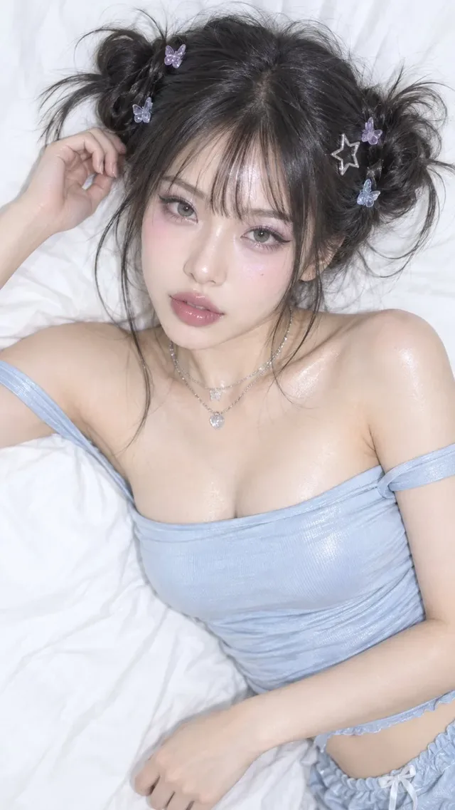 Overhead view of a young East Asian woman with dewy skin and glossy makeup, wearing an icy blue off-shoulder top and double space buns, looking directly at the camera.