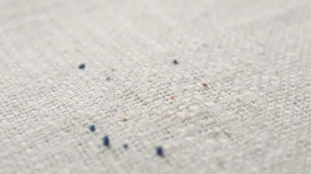 Extreme macro shot of colorful threads self-weaving into satin stitches on a woven cotton shirt fabric to form a logo.