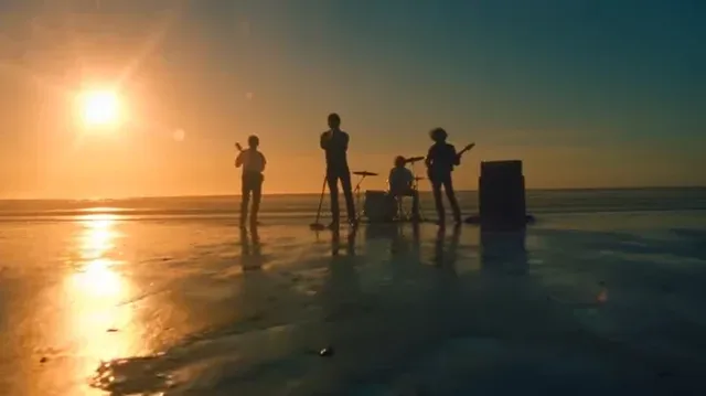 Cinematic hip-hop music video scene on a beach at sunset. A band performs with waves crashing behind them, illuminated by golden light. Close-ups show energetic singing and playing, with quick cuts.