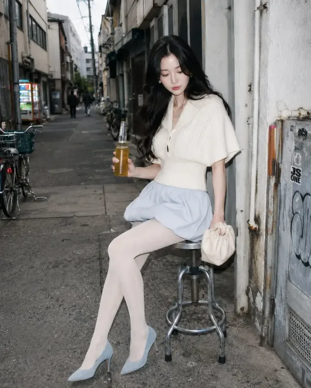 A stylish winter outfit with a cream cable-knit capelet top, pale blue miniskirt, cream tights, powder-blue pumps, and a cream pouch bag.