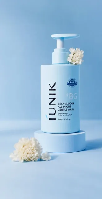 A single baby-blue skincare pump bottle stands on a pedestal with soft white flowers beside it, against a gradient blue background.