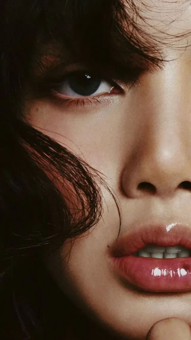 Extreme close-up macro beauty portrait of a young East Asian woman. One eye is in sharp focus, with glossy lips slightly parted. Tousled black hair frames the face. Soft studio lighting.