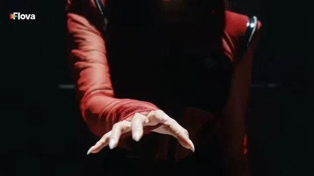A K-pop idol in a striking red and black outfit is dramatically lit by spotlights, performing intense choreography against a crimson backdrop with theatrical fog.
