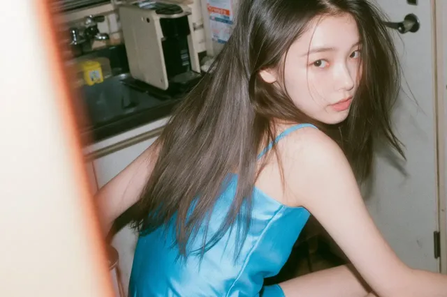 Waist-up, back view portrait of a seductive young Japanese/Korean woman in a neon blue satin dress, kneeling by an office pantry counter, with a retro, hazy, motion-blurred aesthetic.
