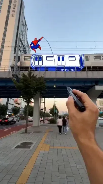 First-person view of a street, holding a marker pen that transforms objects into flat 2D anime characters, with a photorealistic city background.