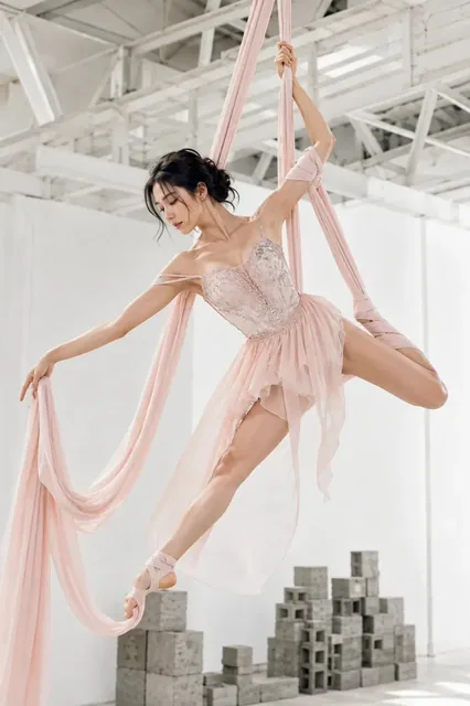 Asian woman in a blush nude couture dress performing an aerial silk split.