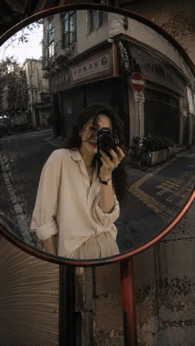A young Chinese woman in casual clothing turns towards the camera with a surprised expression, holding a yellow apple near her chin, standing next to a dark blue bicycle on a street corner. A cinema marquee is visible in the background.