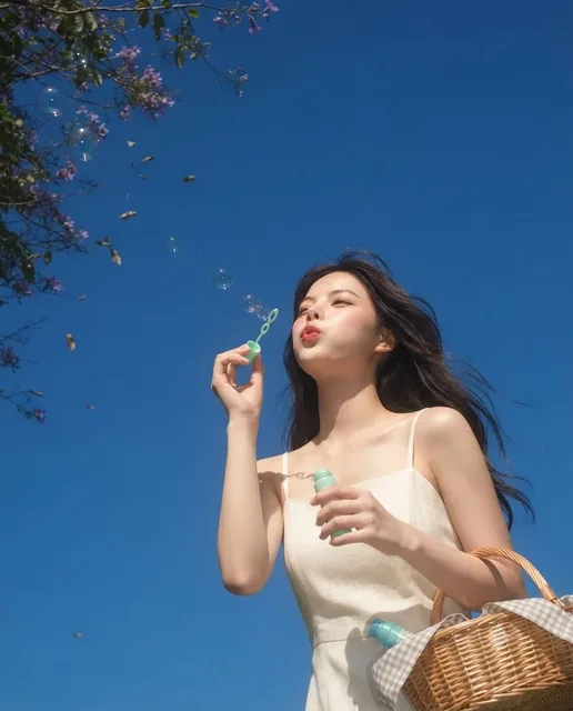 A young girl with eyes closed, blowing soap bubbles, holding a bubble wand and a picnic basket, captured with a soft, dreamy, vintage digital camera effect.