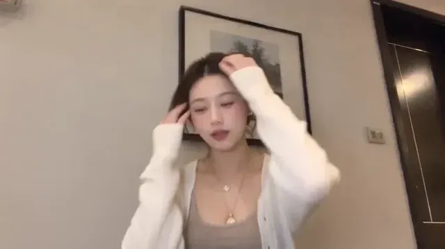 A stylish young woman taking a handheld phone selfie against a white wall, featuring dynamic angles, close-up face shots, and a moody aesthetic.