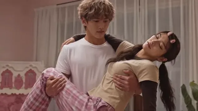 A young man carries a sleeping woman into a pink bedroom, lays her on the bed, tucks her in, and then sleeps on the floor at the foot of the bed.