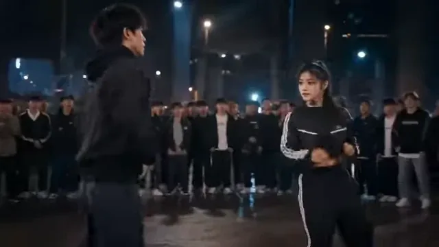 Two young dancers in a street dance battle, one performing a move while the other watches intensely.