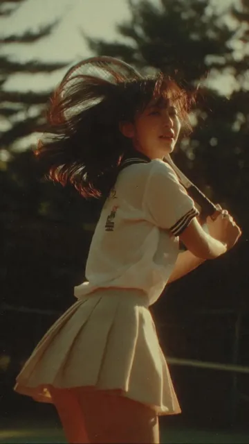 Japanese teenage girl in tennis uniform, captured mid-swing during a match, with soft sunlight and a nostalgic 90s film aesthetic.