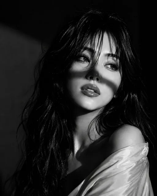 Black and white Vogue editorial portrait of a Japanese woman with wavy hair, wearing an off-shoulder blouse and sparkling earrings, lit with dramatic chiaroscuro lighting.