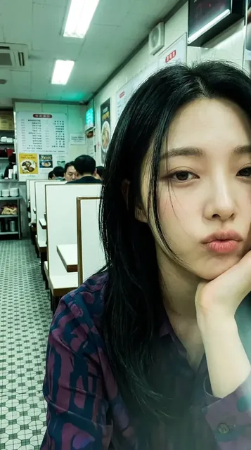 Extreme close-up of a woman's face in the right half of a diner booth, with cluttered background visible on the left. Shot with a grainy, late-90s compact camera effect and a green-cyan cast.