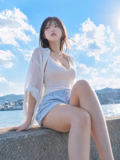 A young woman with dark brown hair, wearing a white tank top and sheer shirt, sits on a concrete seawall with a serene expression, looking towards the sky.